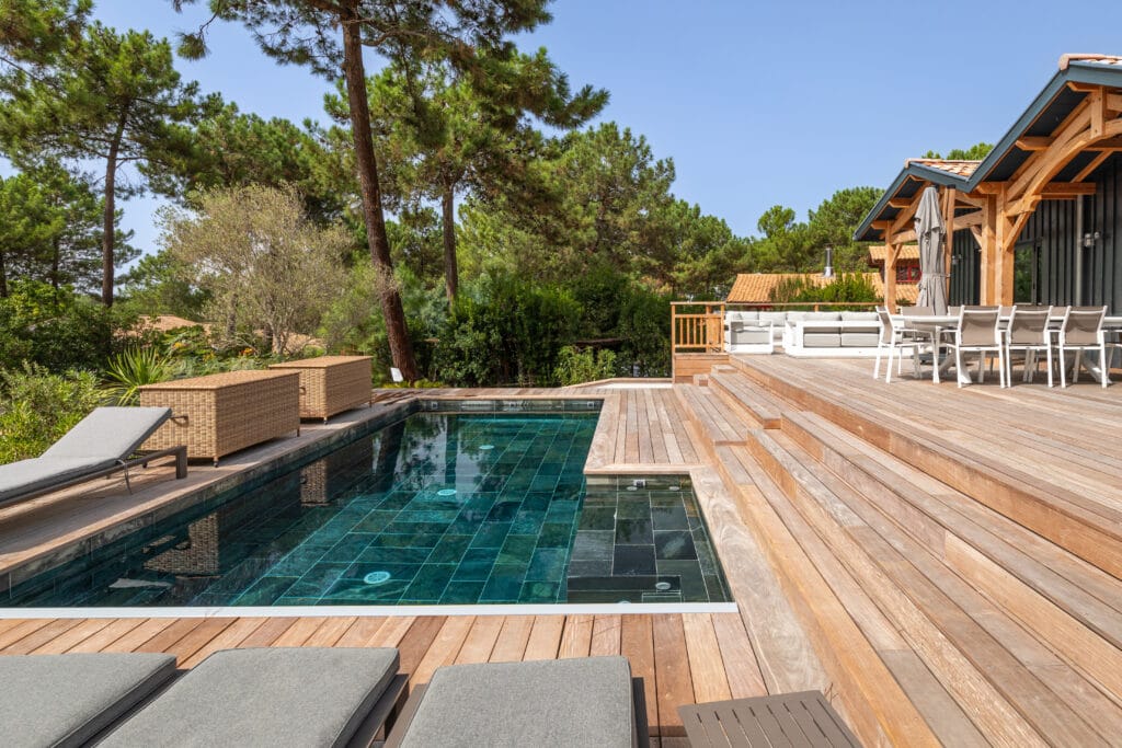 Piscine intégrée à une terrasse en bois dans un jardin arboré